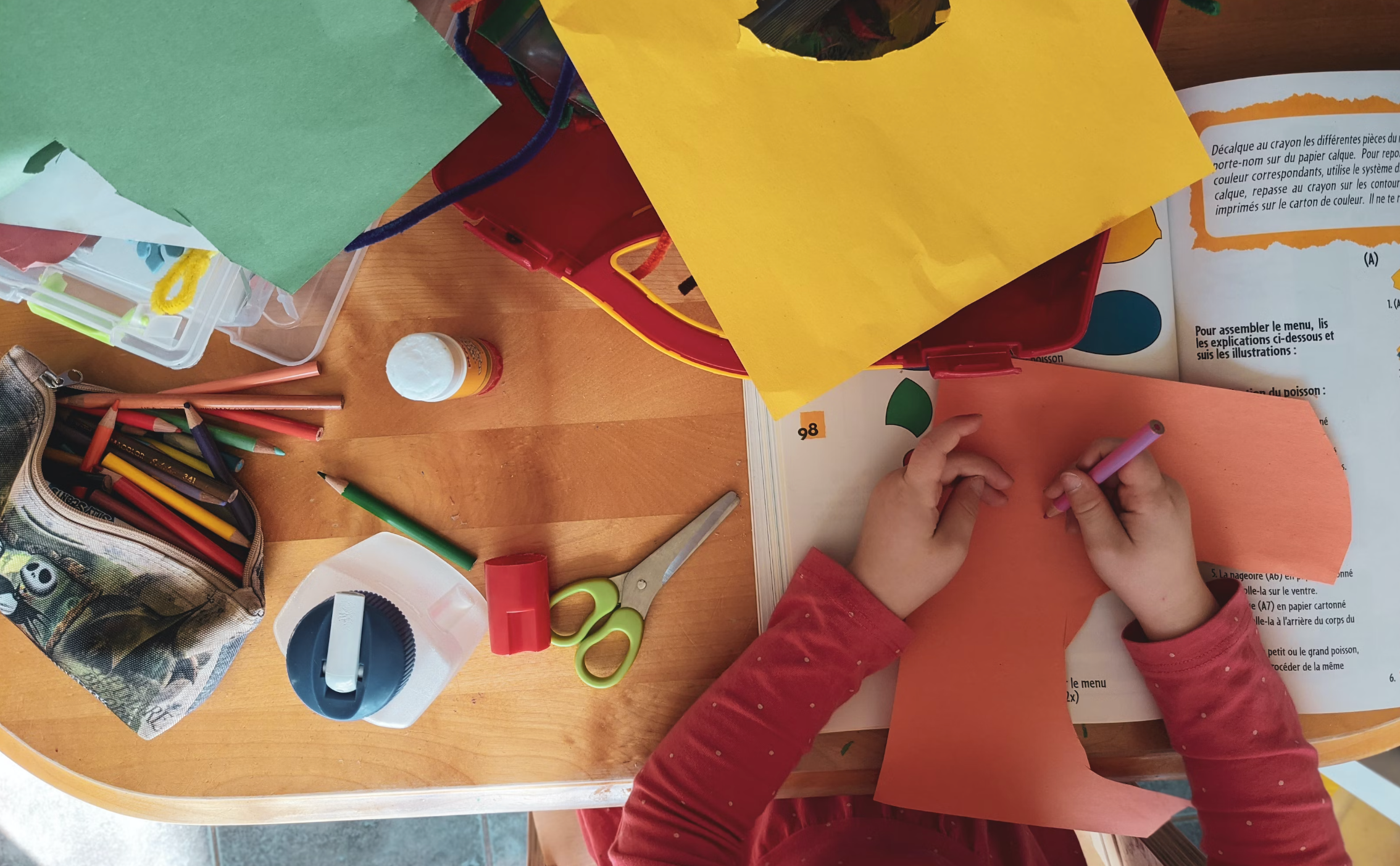 child's hands drawing on construction paper with various art supplies around the table